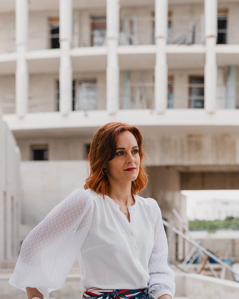 Alexandra Durand assise sur un chantier de logements neufs, devant un immeuble en construction.